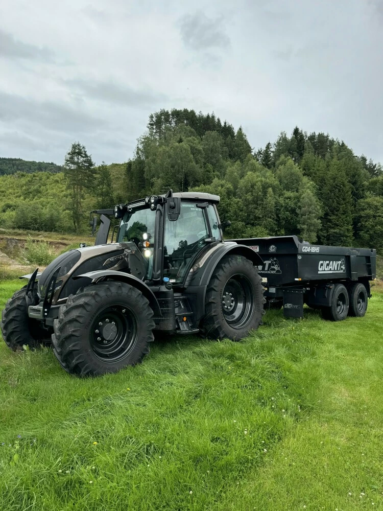 Sort traktor med tilhenger på grønn eng