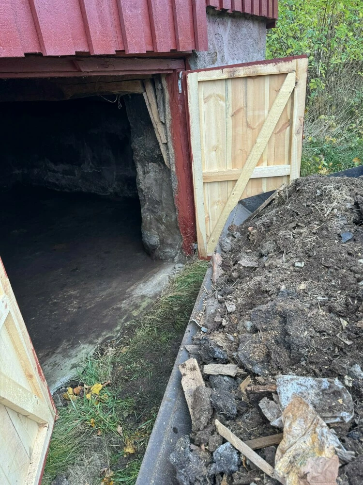 Kjelleråpning med dører og haug av jord og stein